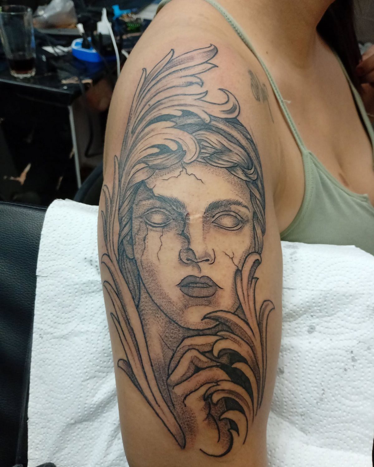 A black and grey tattoo of a cracked marble woman's face on a person's arm.