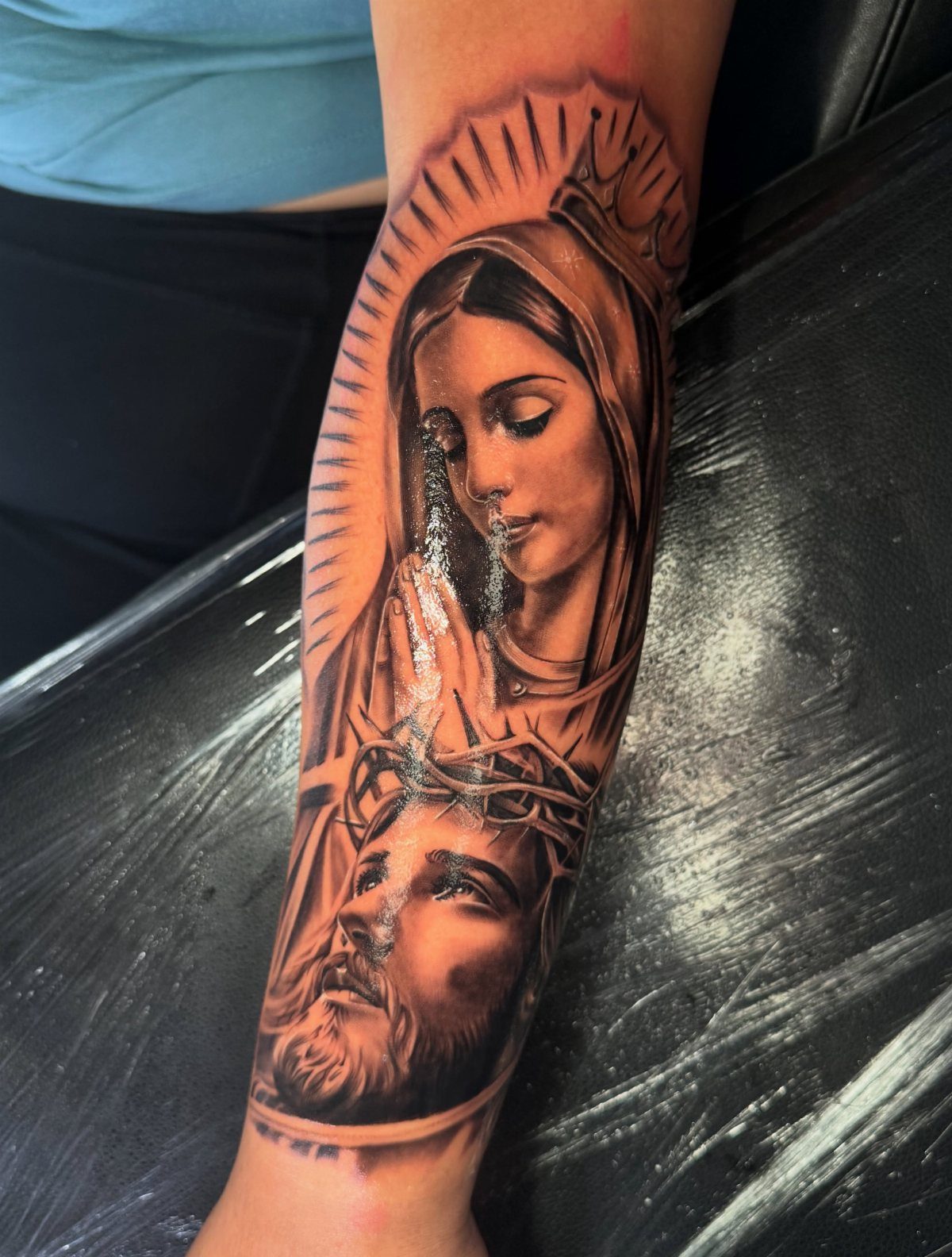 Black and grey realism tattoo of Jesus and Mary on a person's forearm.