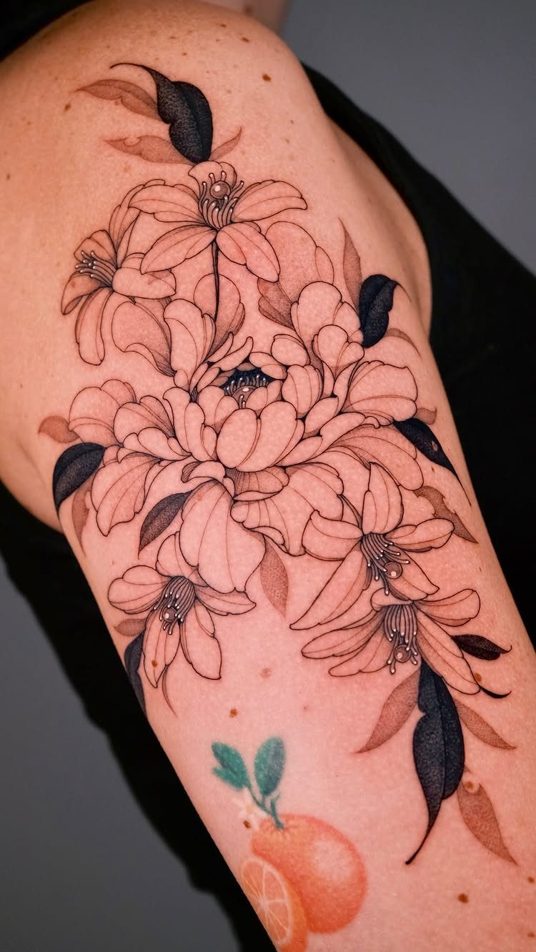 Large peony and lily floral tattoo with grey shading on a person's upper arm.