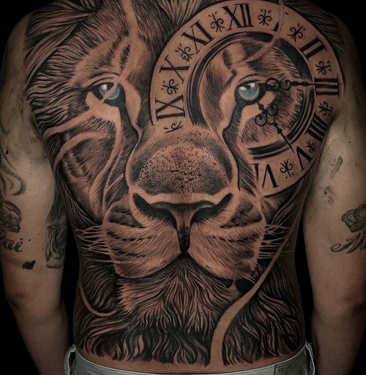 A large black and grey realism tattoo of a lion's face and a Roman numeral clock.