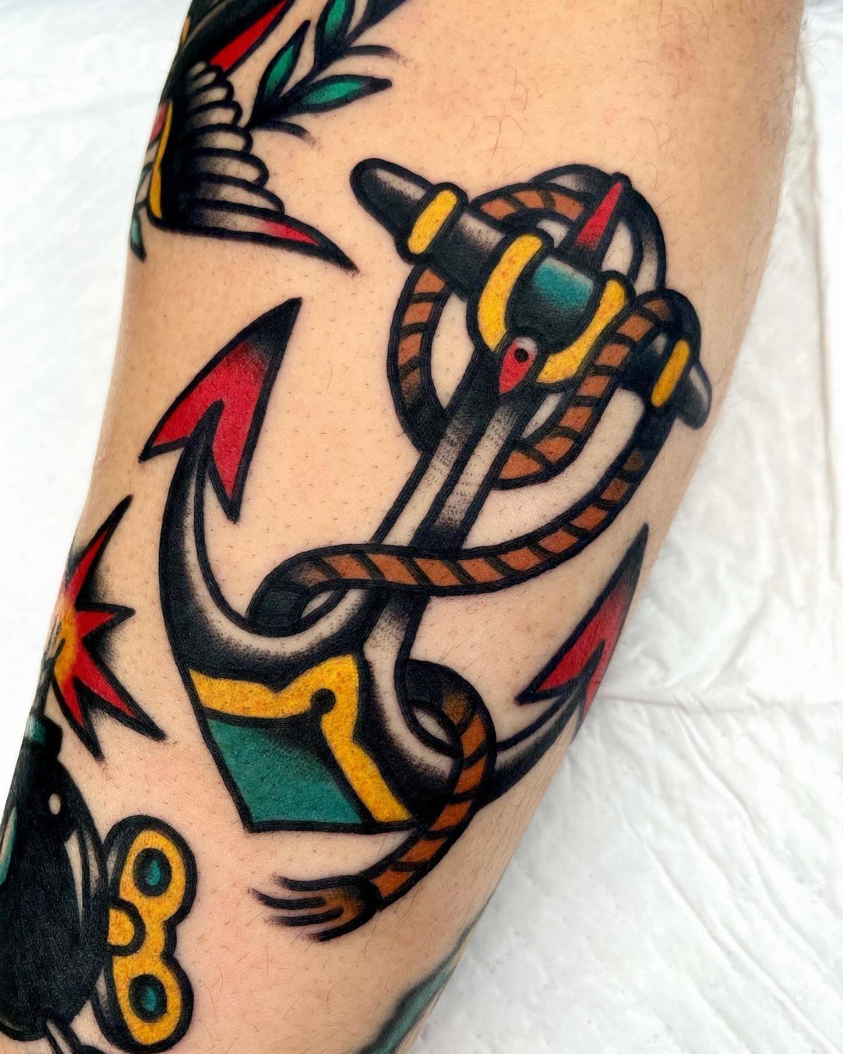 An American traditional anchor tattoo with red tips and a coiled rope on skin.