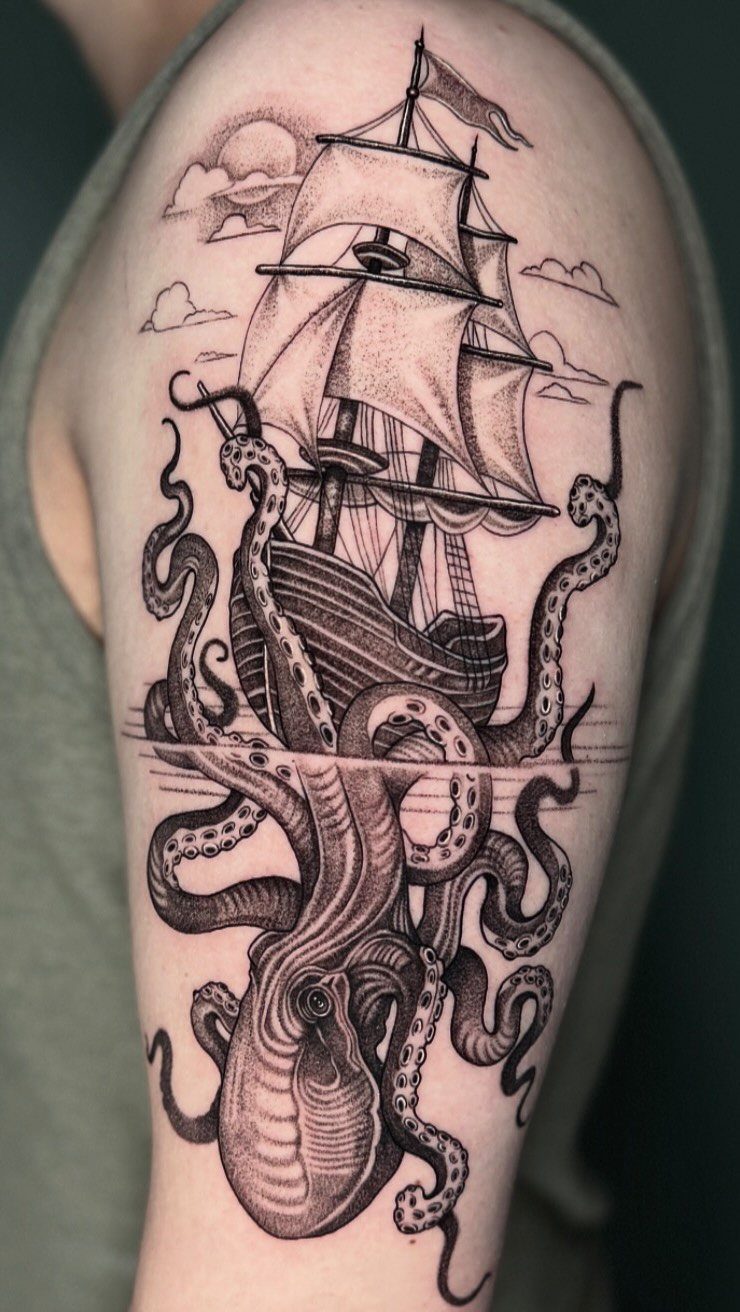 A black and grey tattoo of a sailing ship entwined by an octopus tentacles on an arm.
