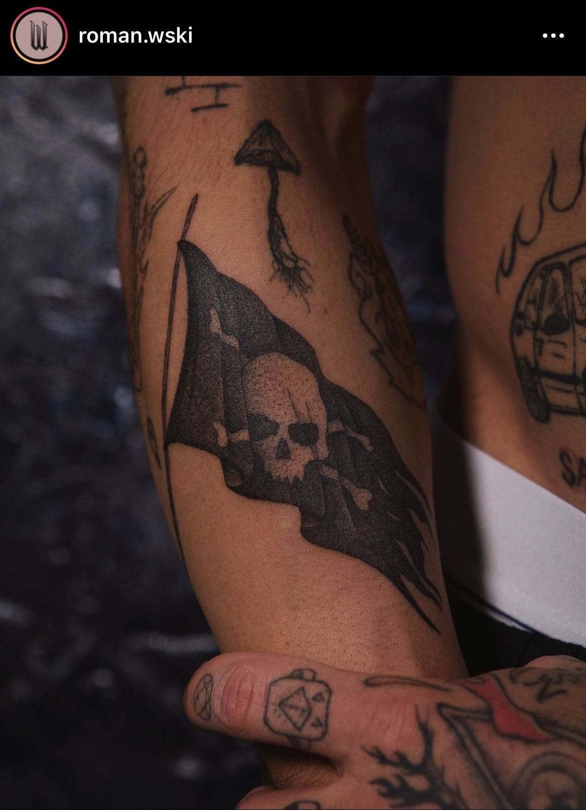 A black ink tattoo of a pirate flag with a skull and crossbones on a person's arm.