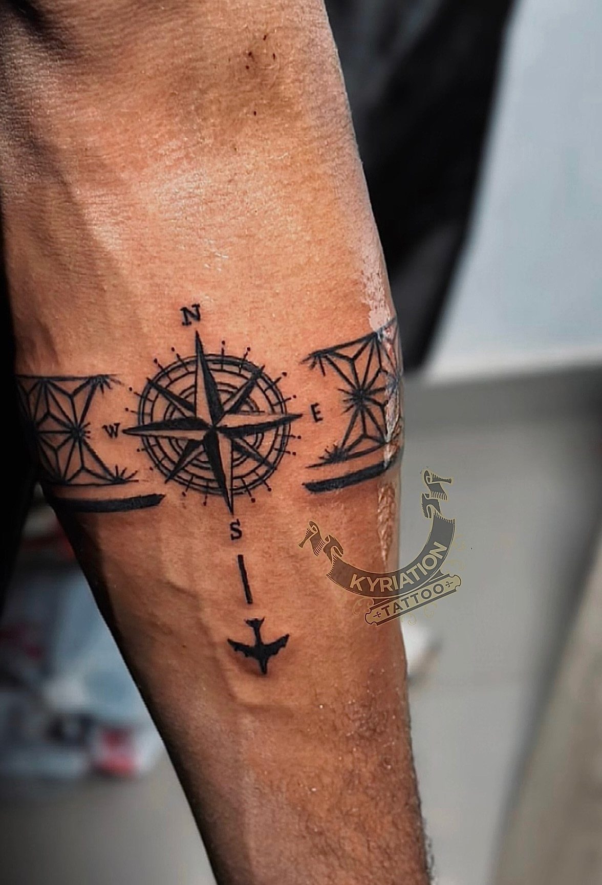 A black ink compass rose tattoo with geometric patterns wrapping around a person's forearm.