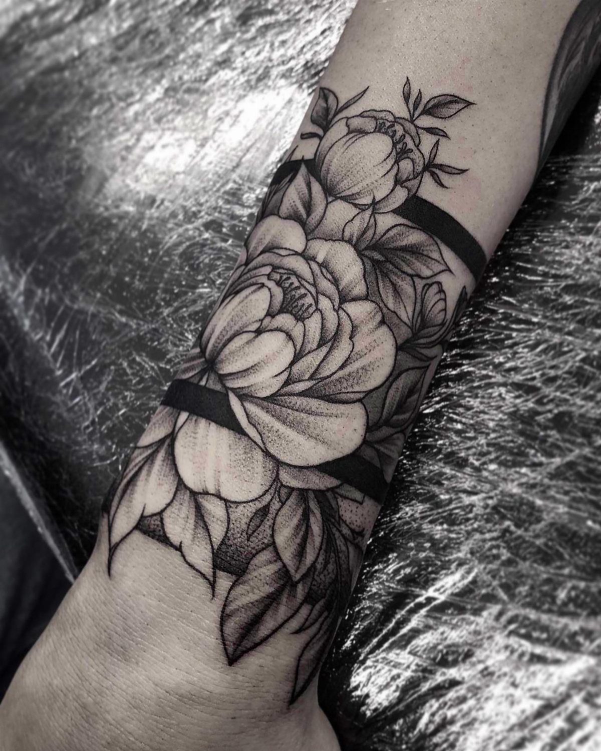 Black and grey peony tattoo with thick black bands wrapping around a person's forearm.