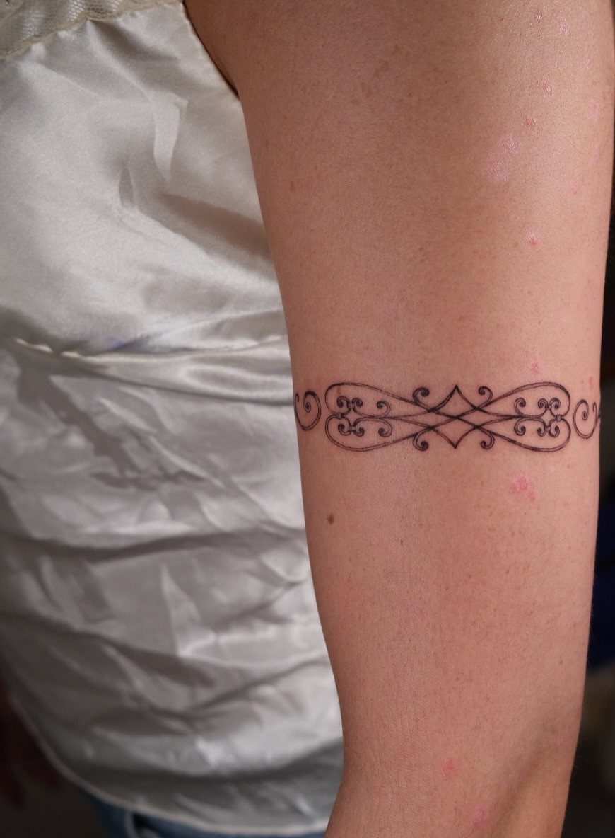 A black ink scrollwork band tattoo encircling a person's upper arm.