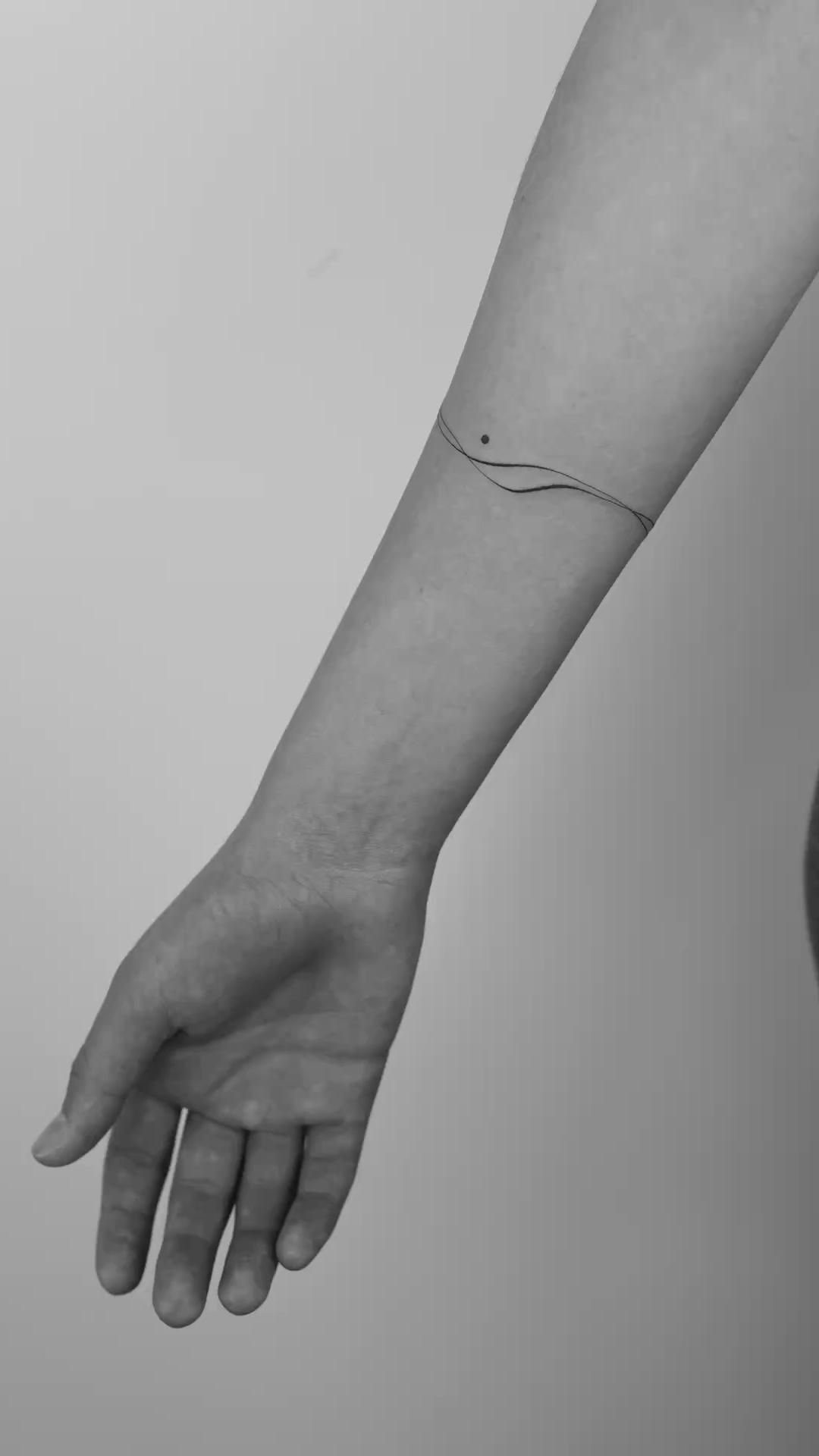 A thin black ink line tattoo encircling a person's wrist on a pale forearm.