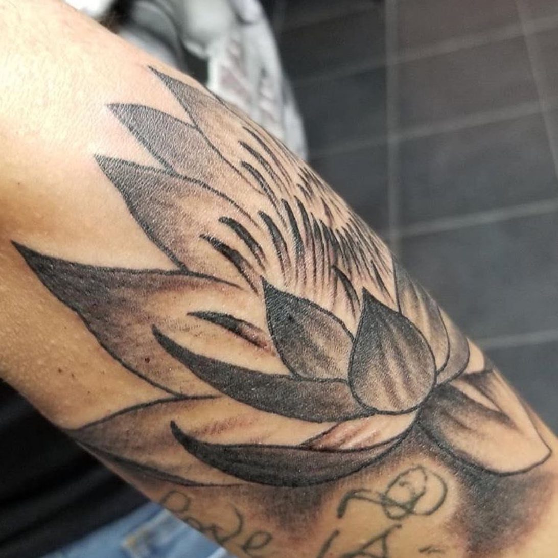 A black and grey water lily tattoo with detailed shading on a person's arm.