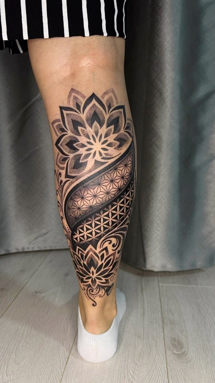 A large black and grey geometric lotus tattoo covering a person's lower leg.