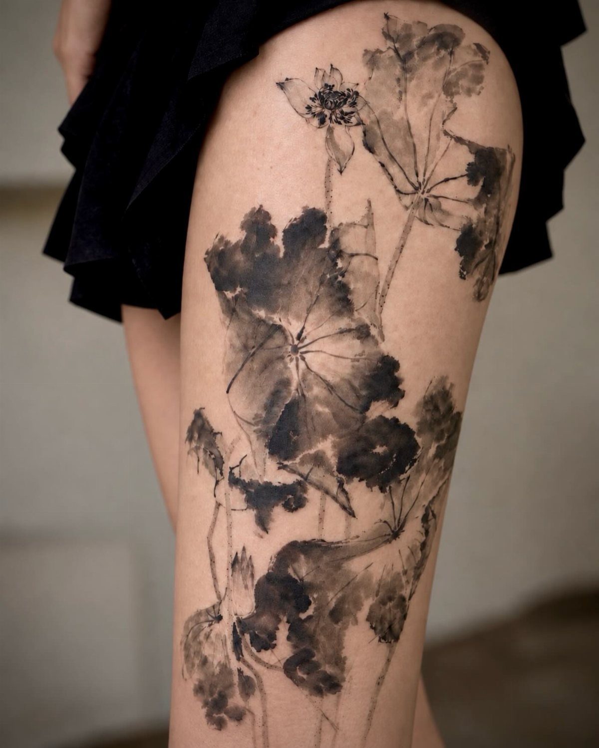 Black and grey water lily tattoo with soft shading on a person's thigh.
