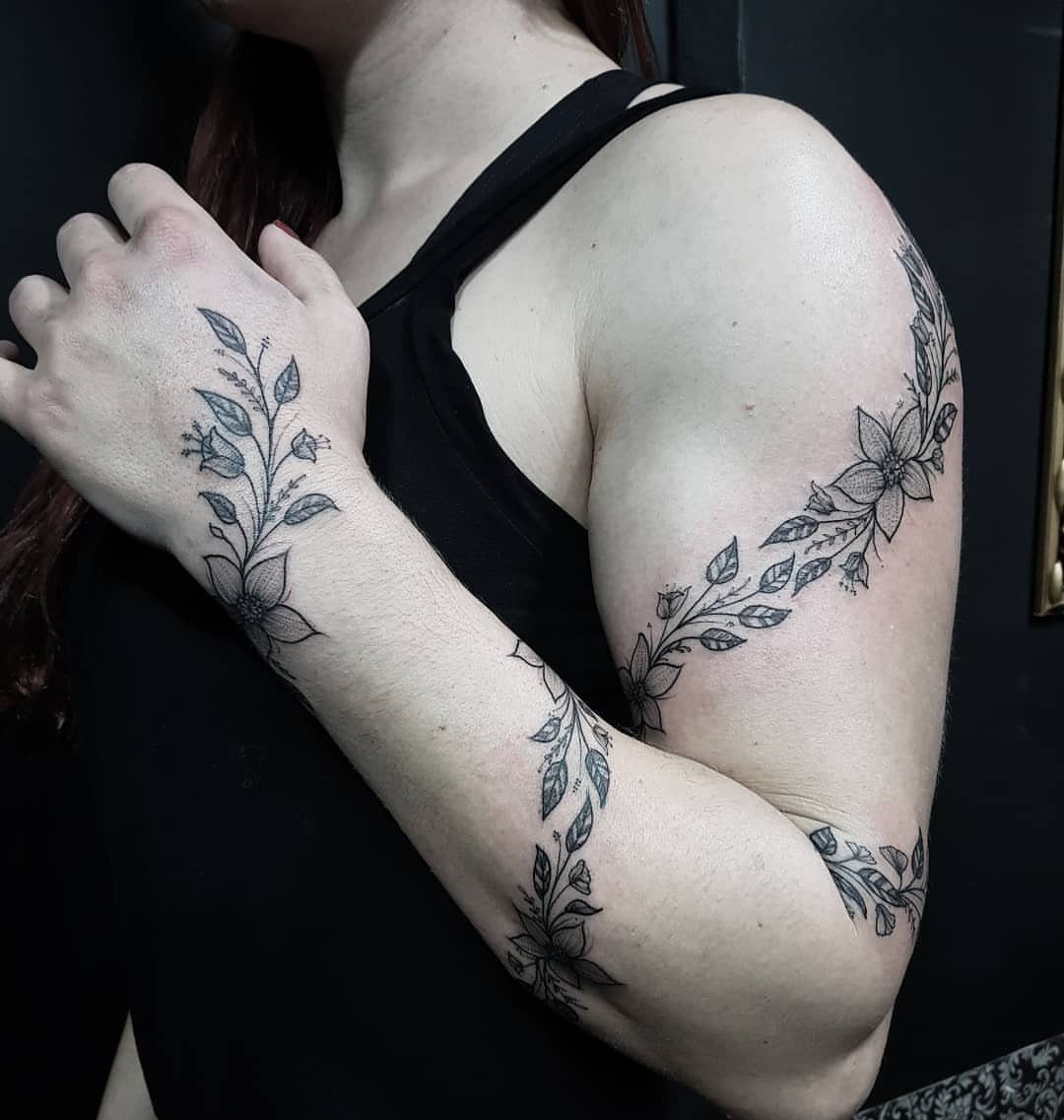 Black ink floral tattoos of leaves and flowers winding around a person's arm and hand.