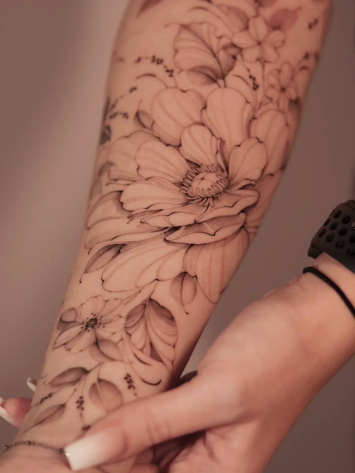 A large floral tattoo with fine line work covering a person's forearm.