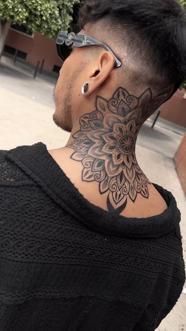 A man with a large black mandala floral tattoo on his neck and upper back.