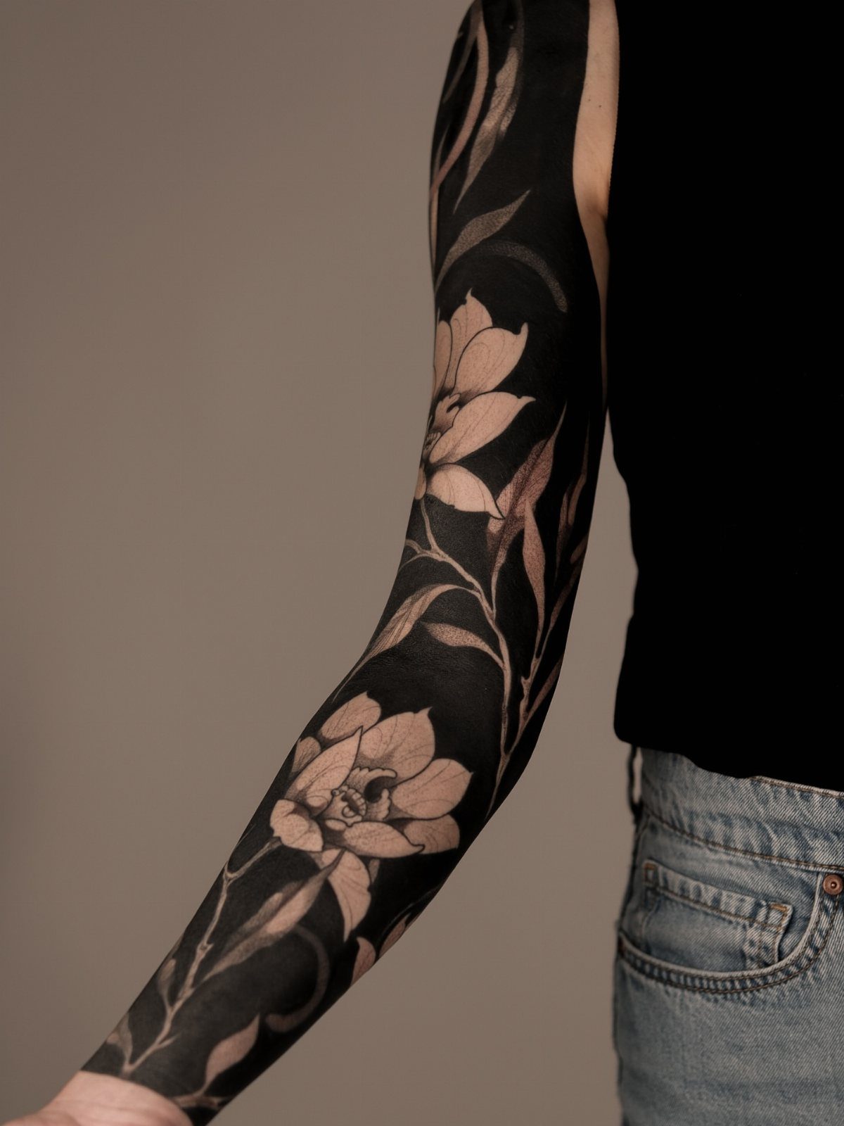 A person's arm covered in a large blackwork floral tattoo with heavy black shading.