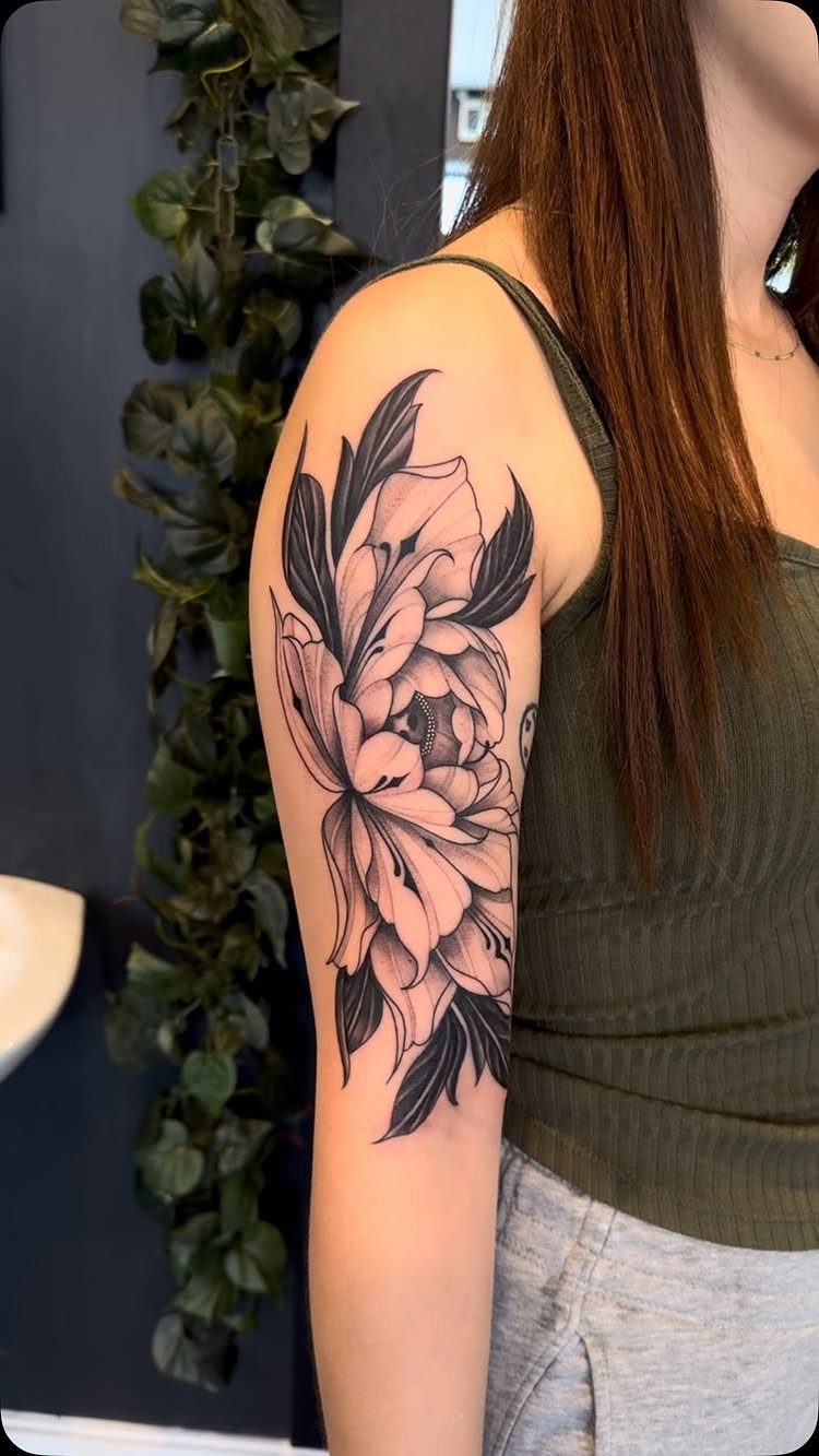 A large black ink peony flower tattoo with leaves on a person's upper arm.