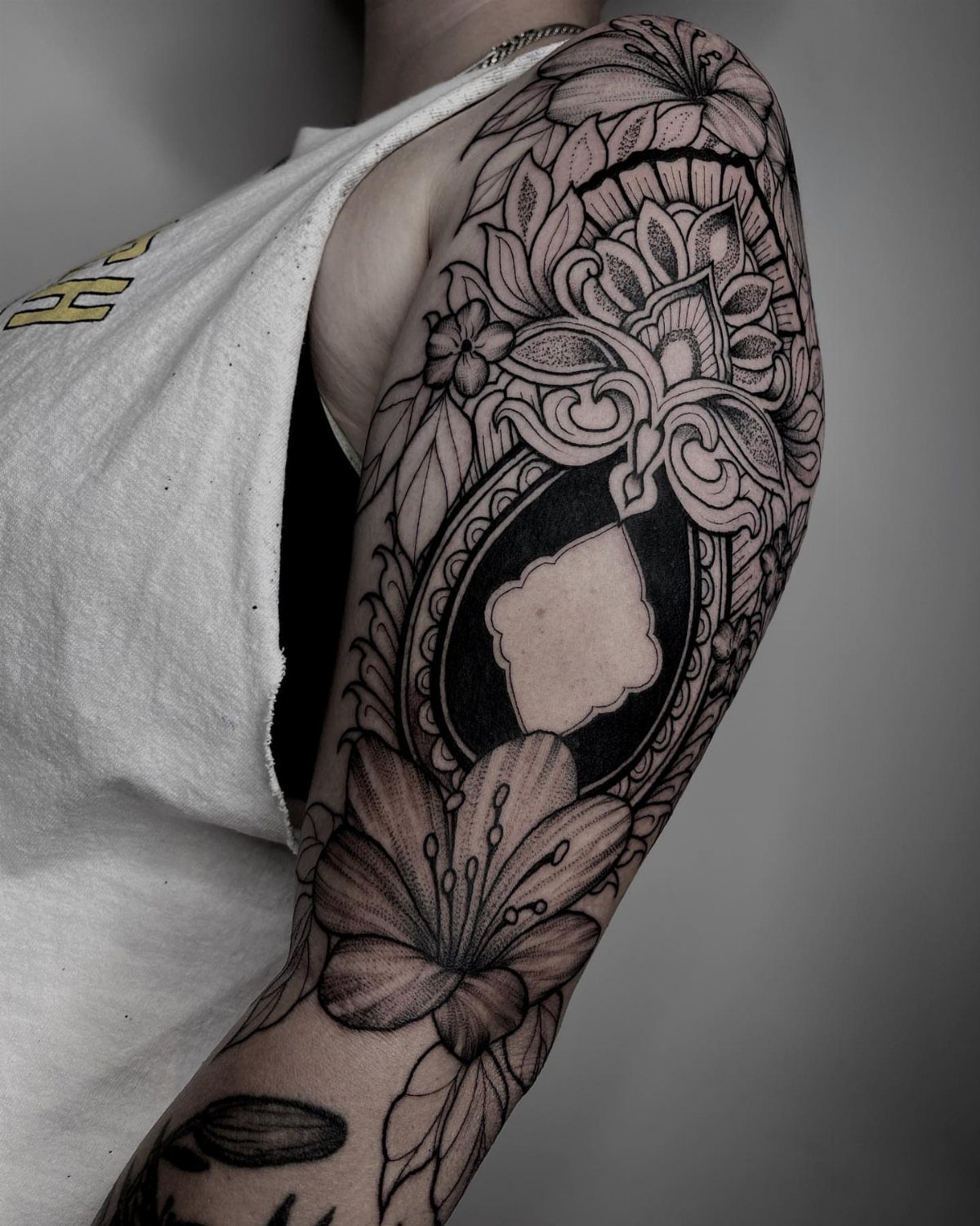 A detailed blackwork tattoo on an arm featuring flowers and intricate ornamental swirls.