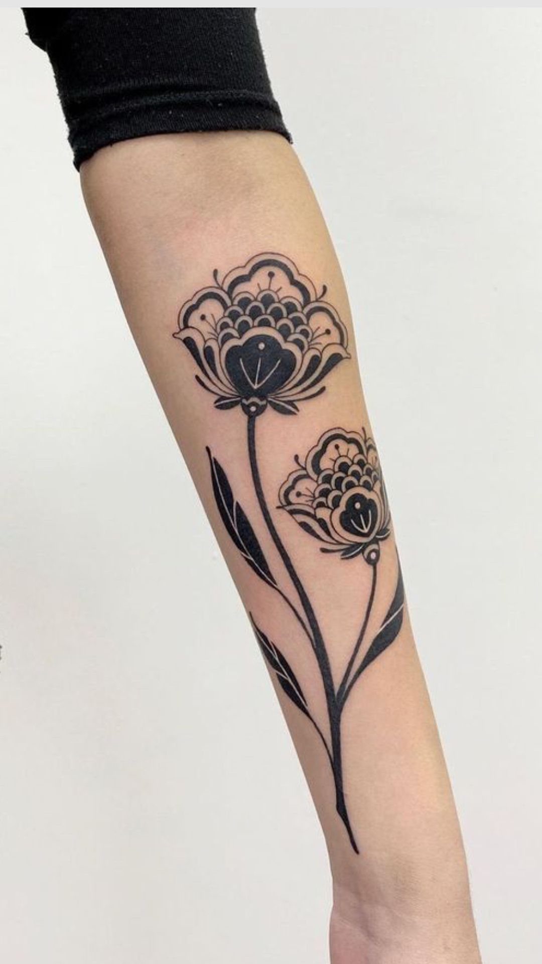 Black ink floral tattoo with two patterned flowers and long stems on a forearm.
