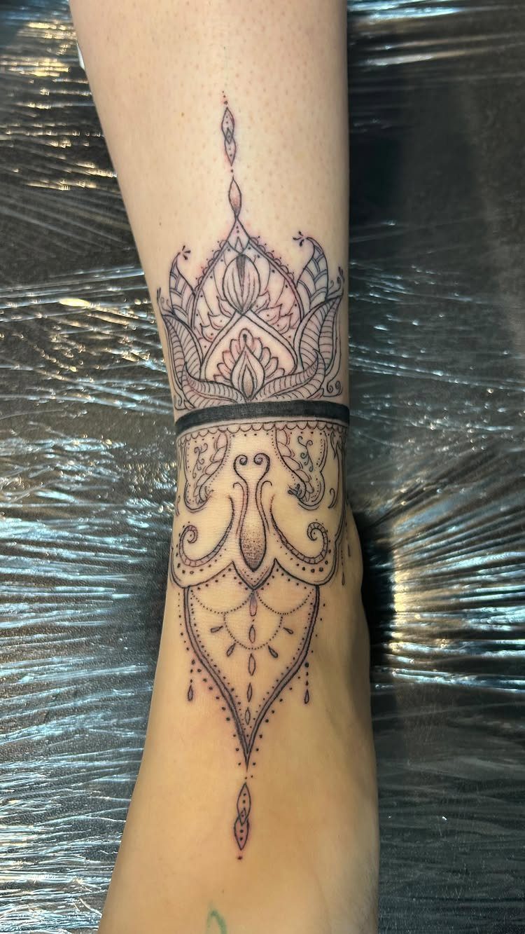 A detailed black ink mandala tattoo wrapping around a person's ankle and lower leg.