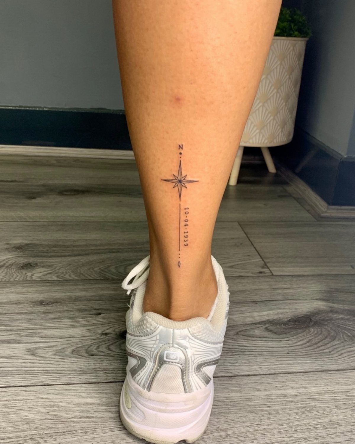 A small black ink compass rose tattoo on a person's lower leg above the ankle.