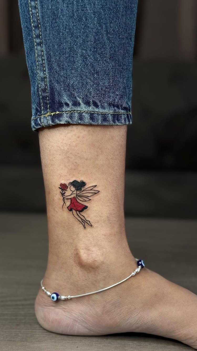 A small fairy tattoo with red clothing and wings on a person's ankle.