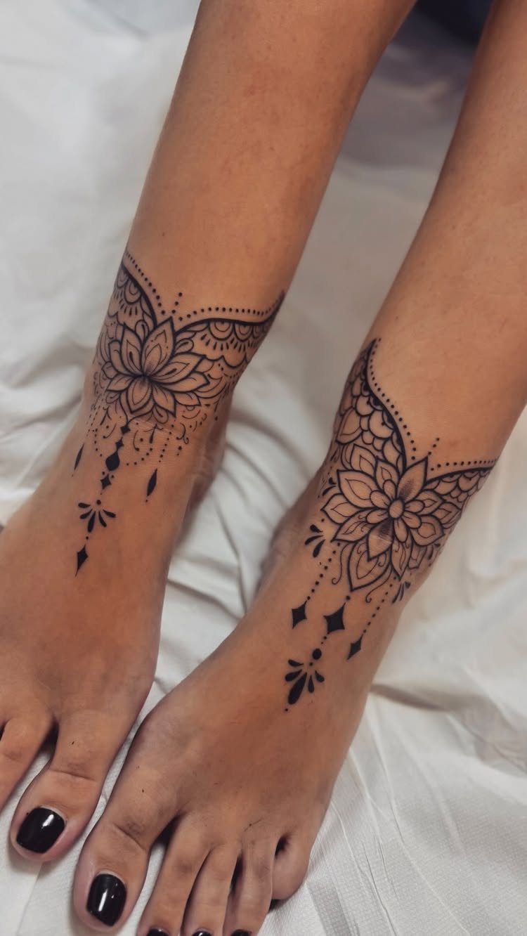 Two feet with intricate black ink mandala tattoos wrapped around the ankles.