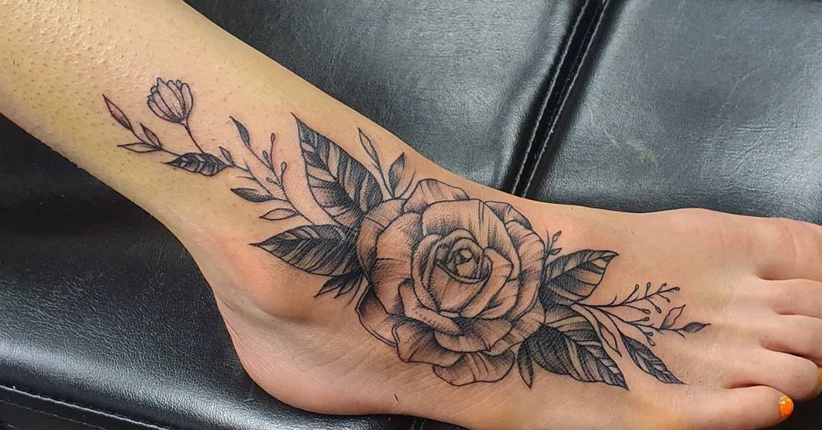 A large black and grey rose tattoo with leaves on a person's foot.