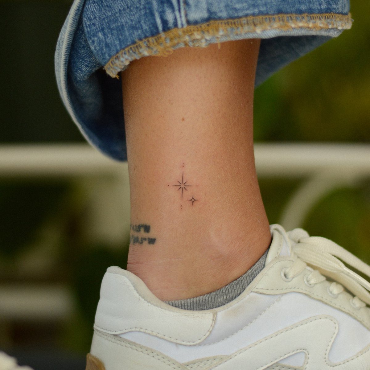 Two small minimalist star tattoos on a person's ankle near white sneakers.