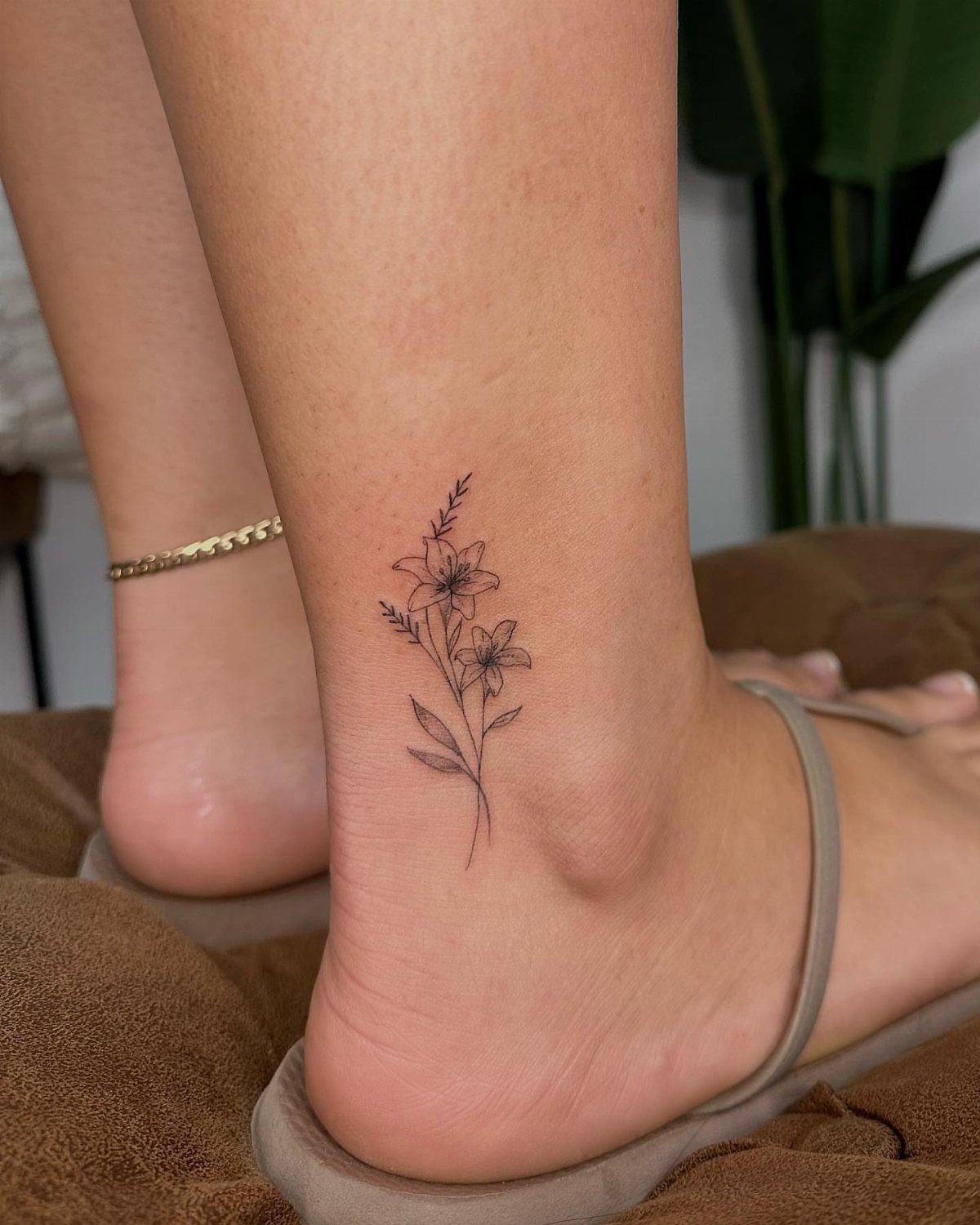 A delicate small black ink floral tattoo on a person's ankle skin.