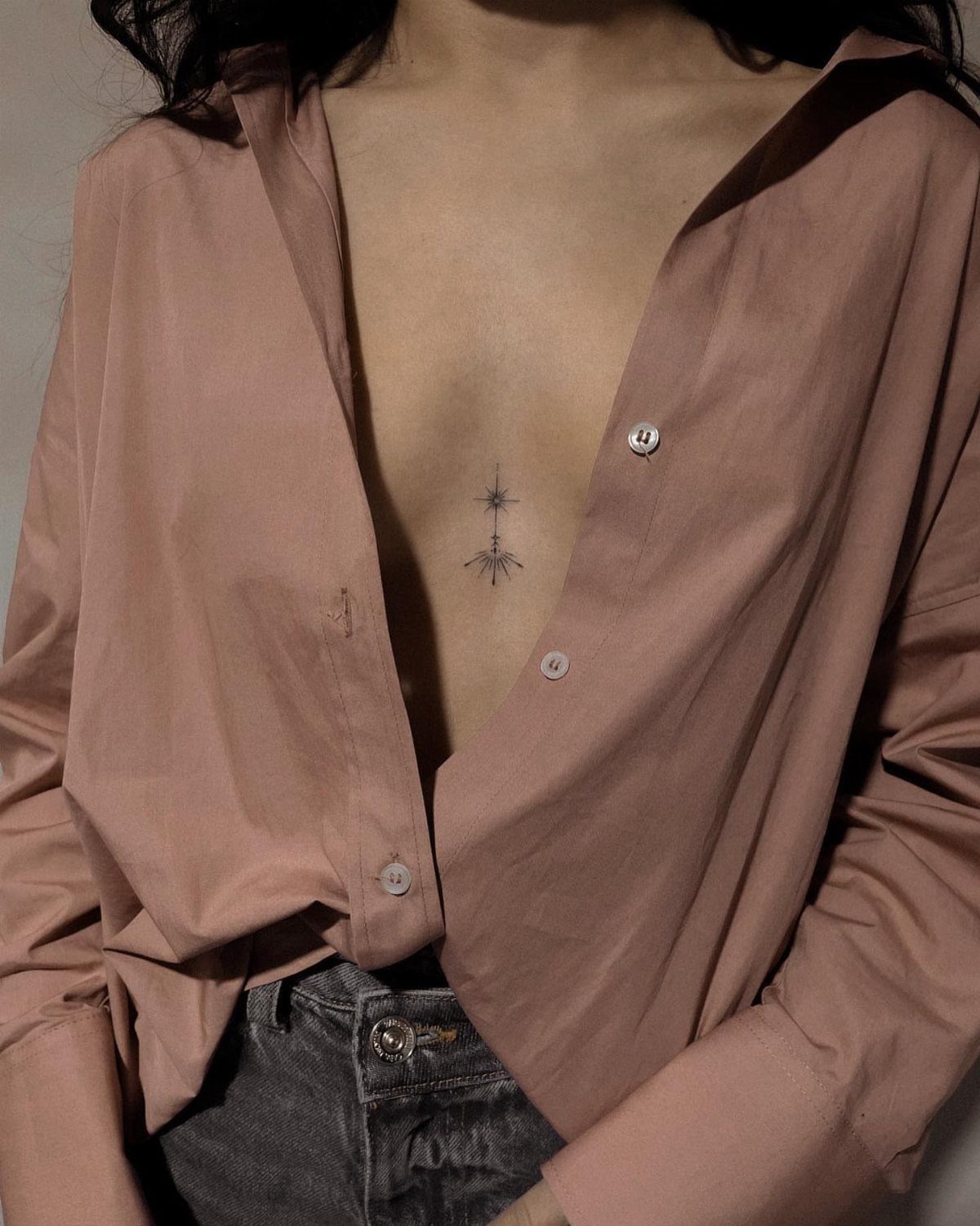 A small starburst tattoo on a person's chest visible through an open shirt.