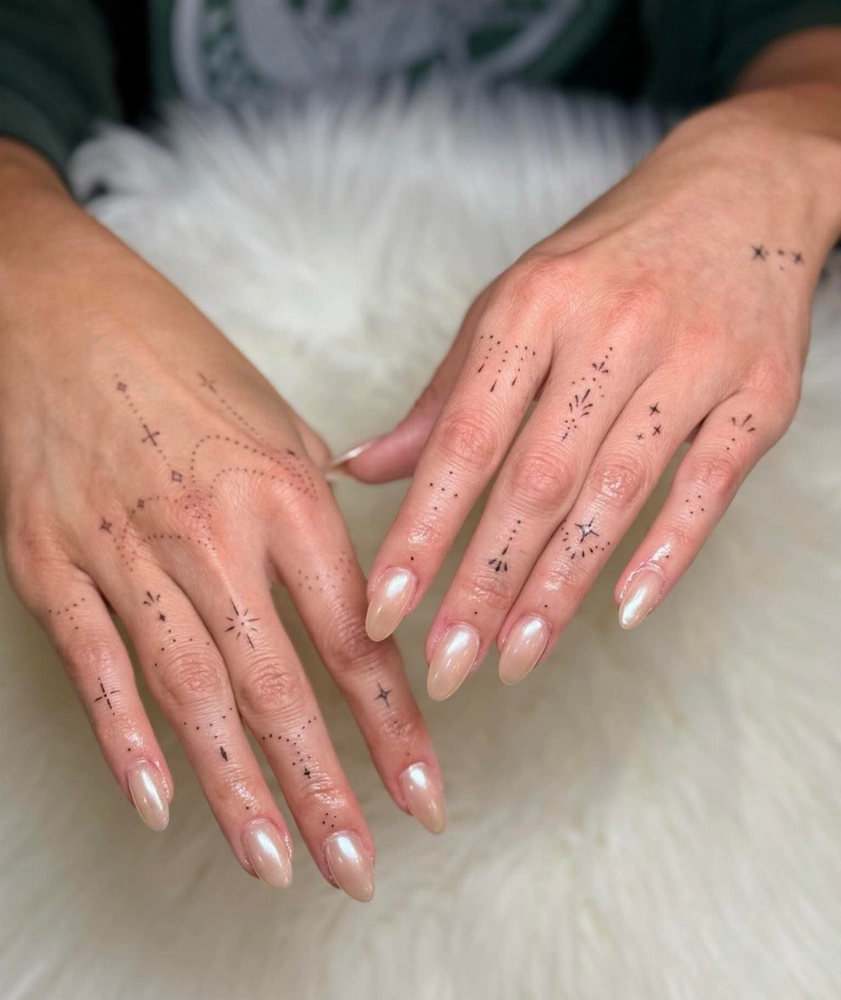 Two hands with dainty star tattoos and long manicured nails resting on white fur.