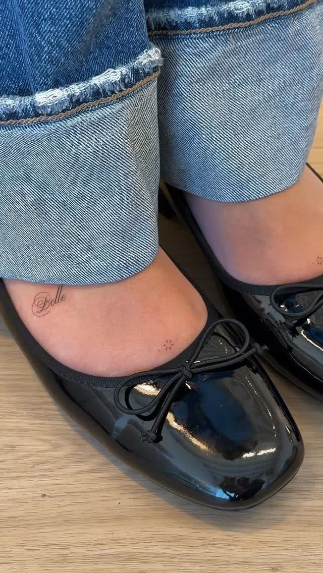 Small script and dot tattoos on the top of a person's foot wearing black ballet flats.