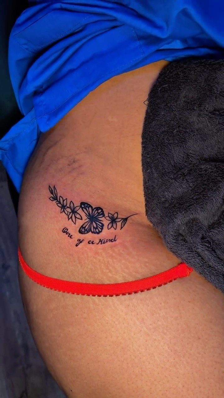 A floral tattoo with script text on a person's hip above a red waistband.