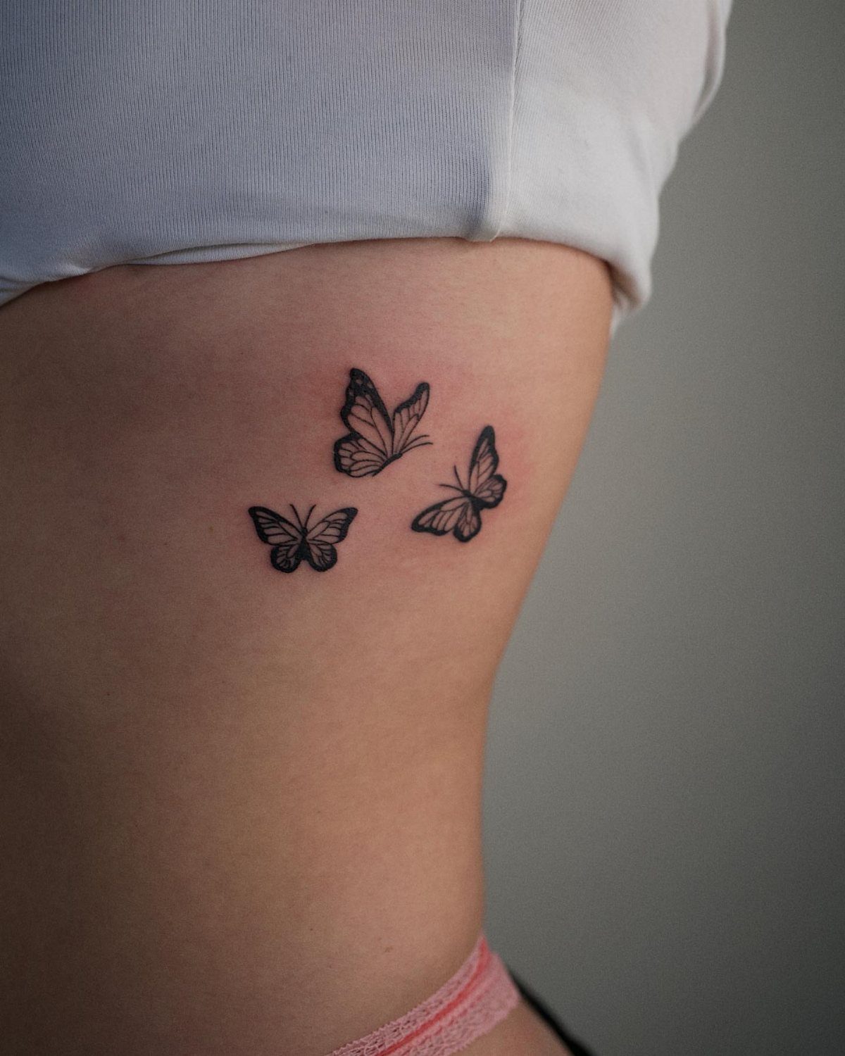 Three small black butterfly tattoos on a person's ribcage side.