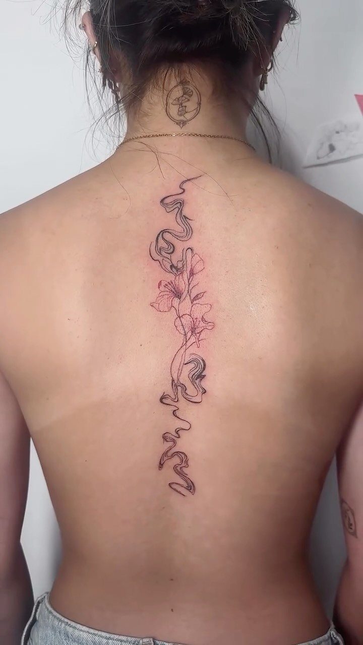 A fine line floral and wavy tattoo running vertically down a person's spine.