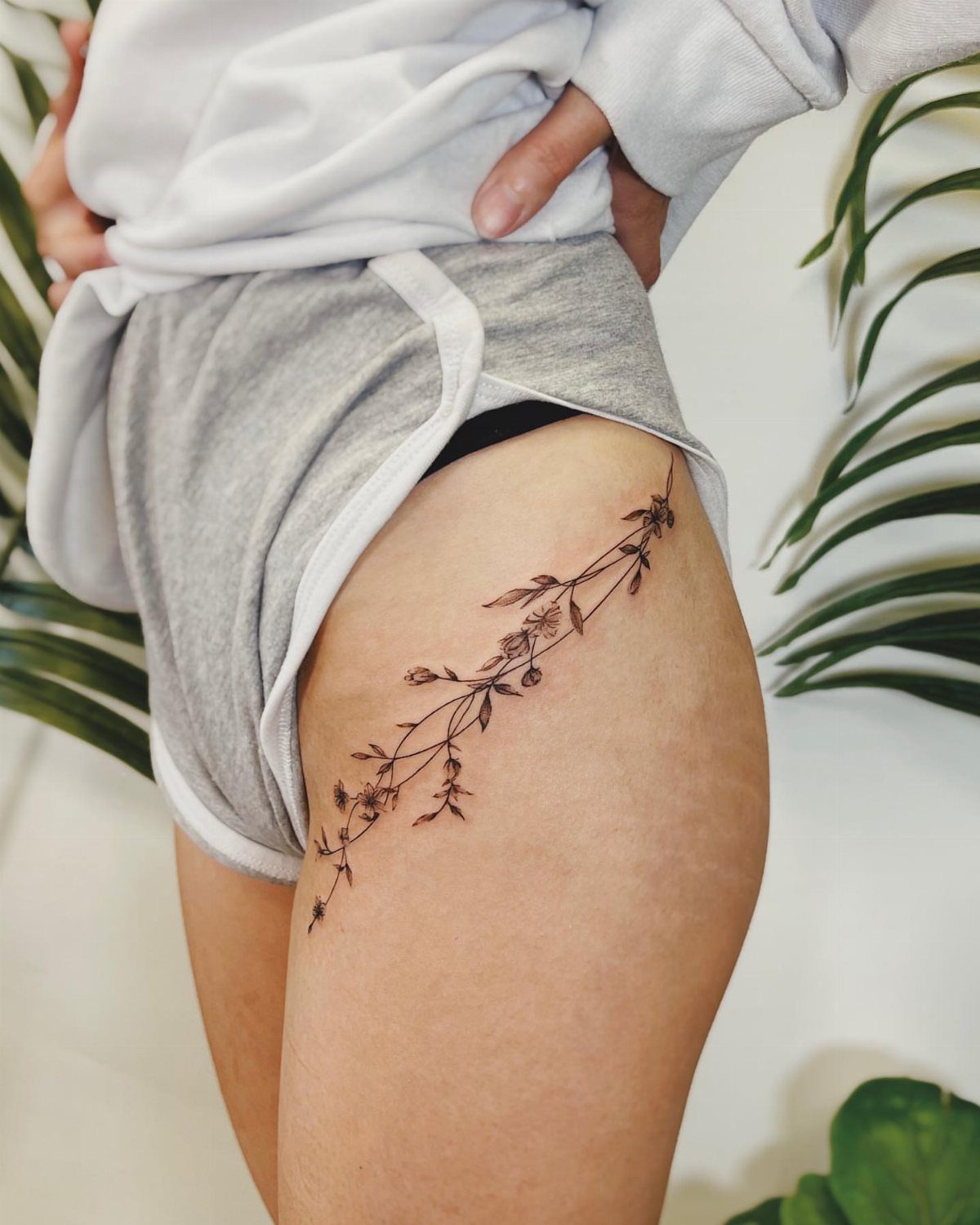 A fine-line floral vine tattoo winding along a person's upper thigh.