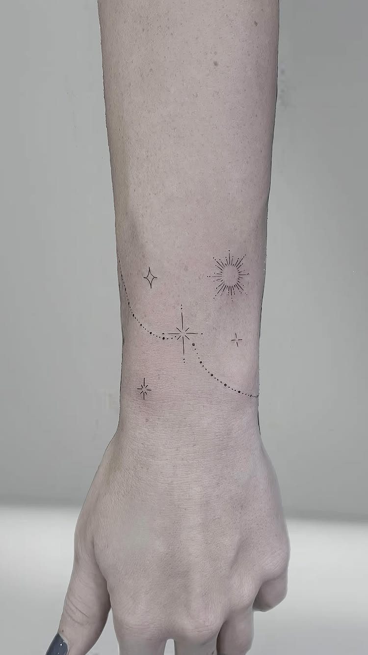 A minimalist line tattoo with stars and a sun on a person's wrist.