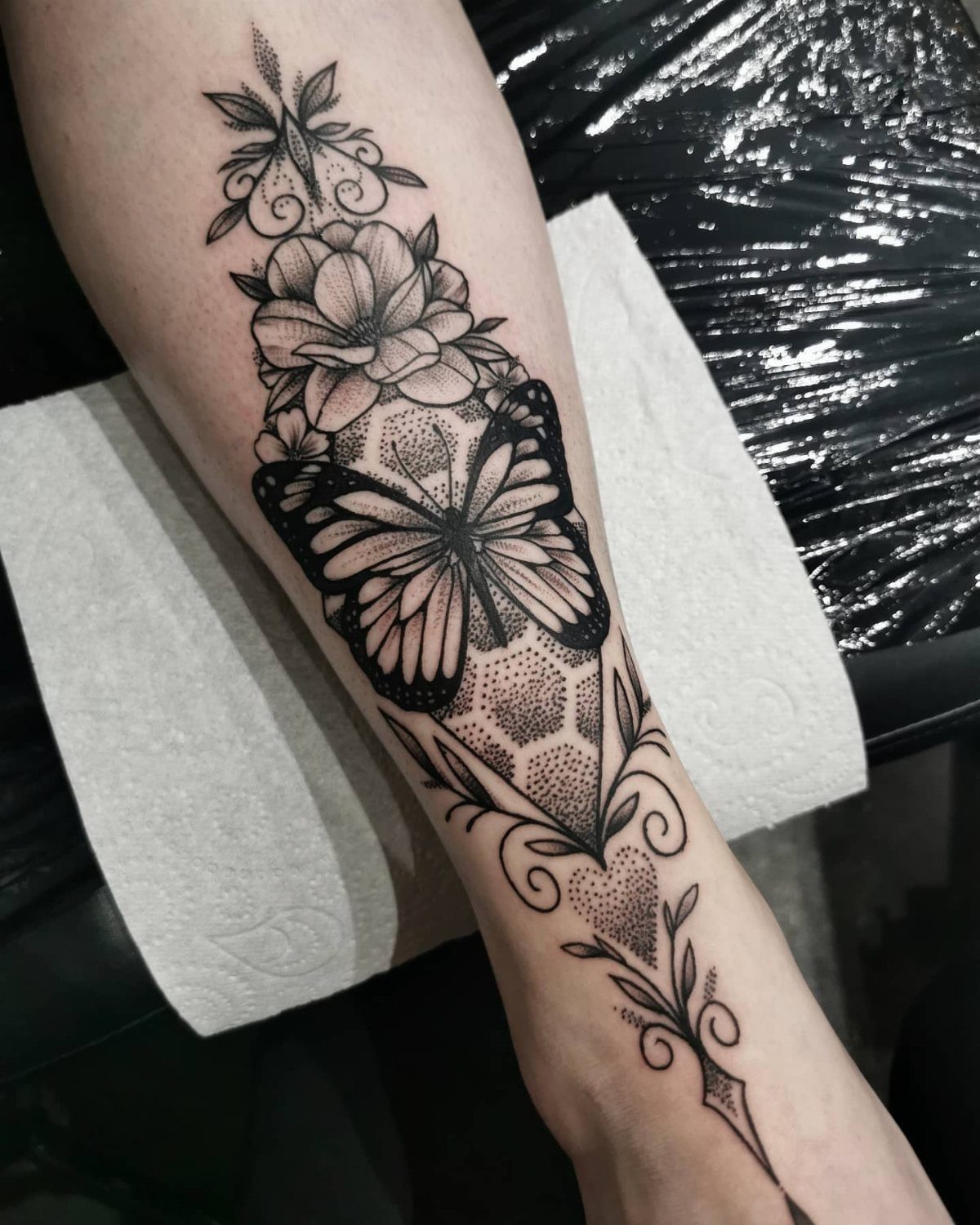 7 Feminine Ankle Tattoos for Every Style 1 A detailed black ink butterfly and floral tattoo on a person's lower leg.