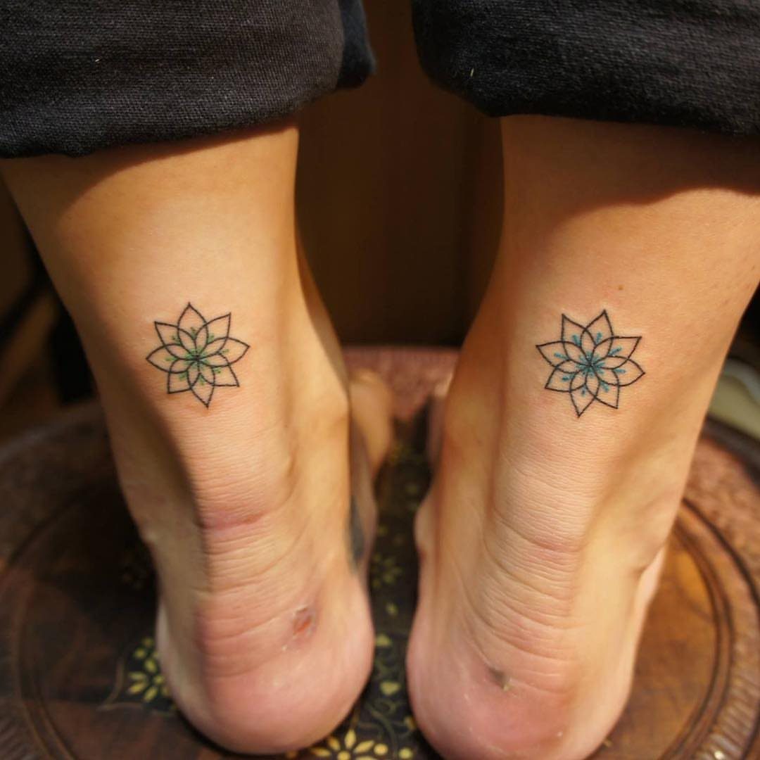 7 Feminine Ankle Tattoos for Every Style 4 Two small geometric mandala tattoos with blue shading on a person's ankles.