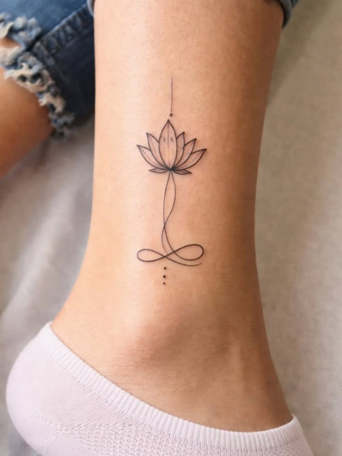 7 Feminine Ankle Tattoos for Every Style 7 A fine line lotus flower and infinity symbol tattoo on a person's ankle.