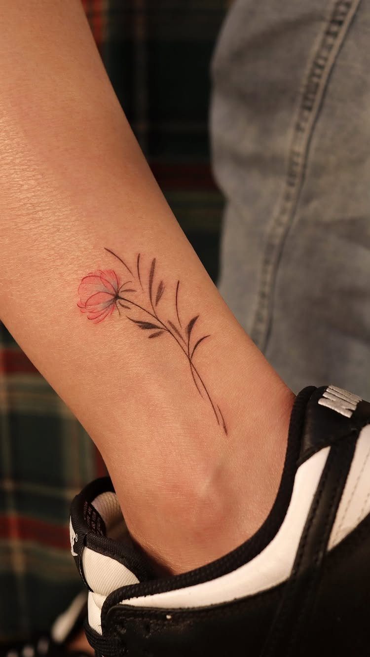 7 Feminine Ankle Tattoos for Every Style 2 A minimalist pink flower tattoo with fine black lines on a person's ankle.