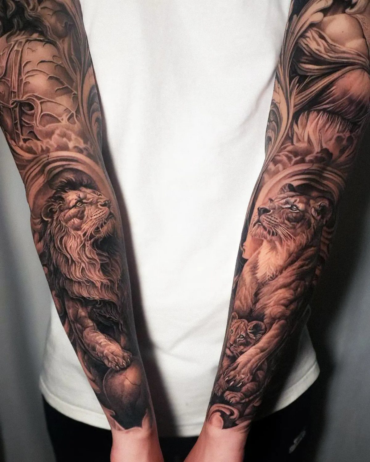 A person showing off full arm sleeve tattoos featuring lions and intricate filigree patterns.