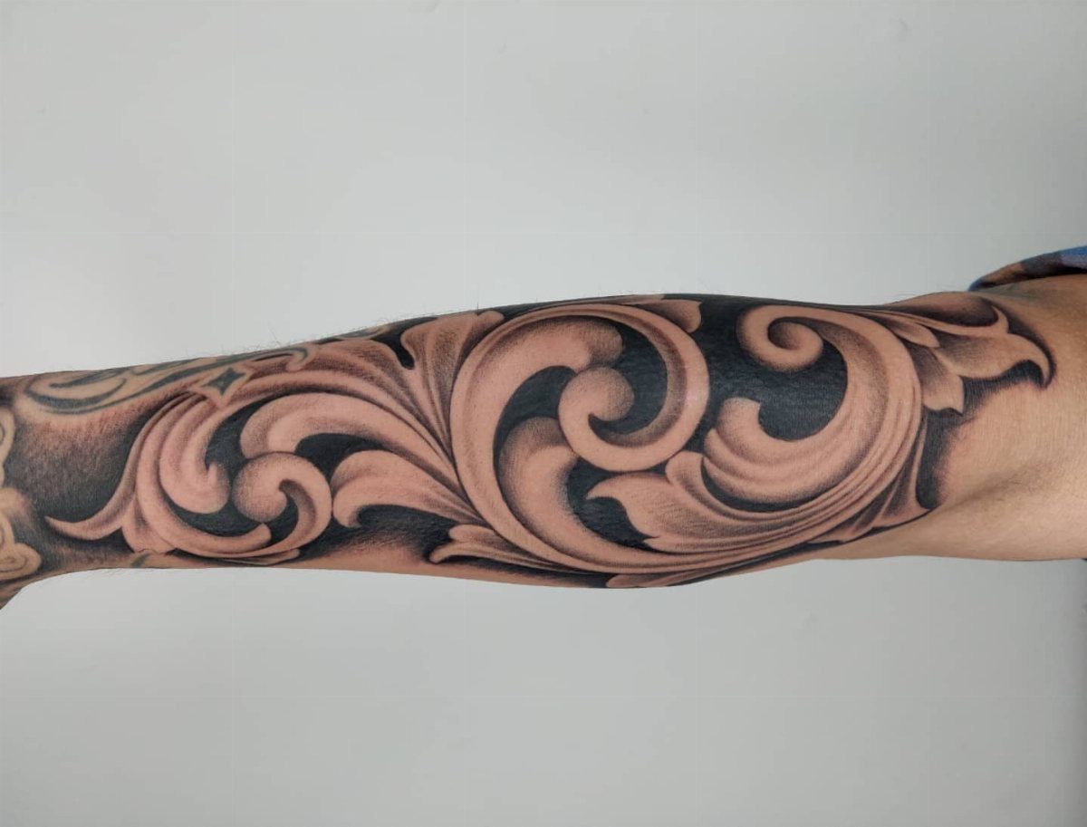 A detailed black and grey tattoo of swirling acanthus leaf patterns on a person's leg.
