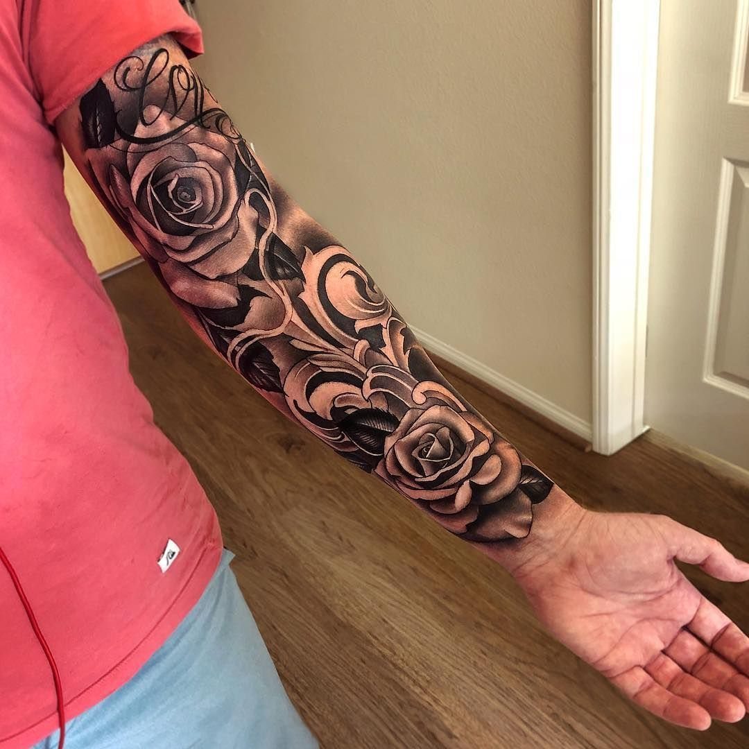 A person's arm displaying a detailed black and grey sleeve tattoo of realistic roses and ornamental filigree.