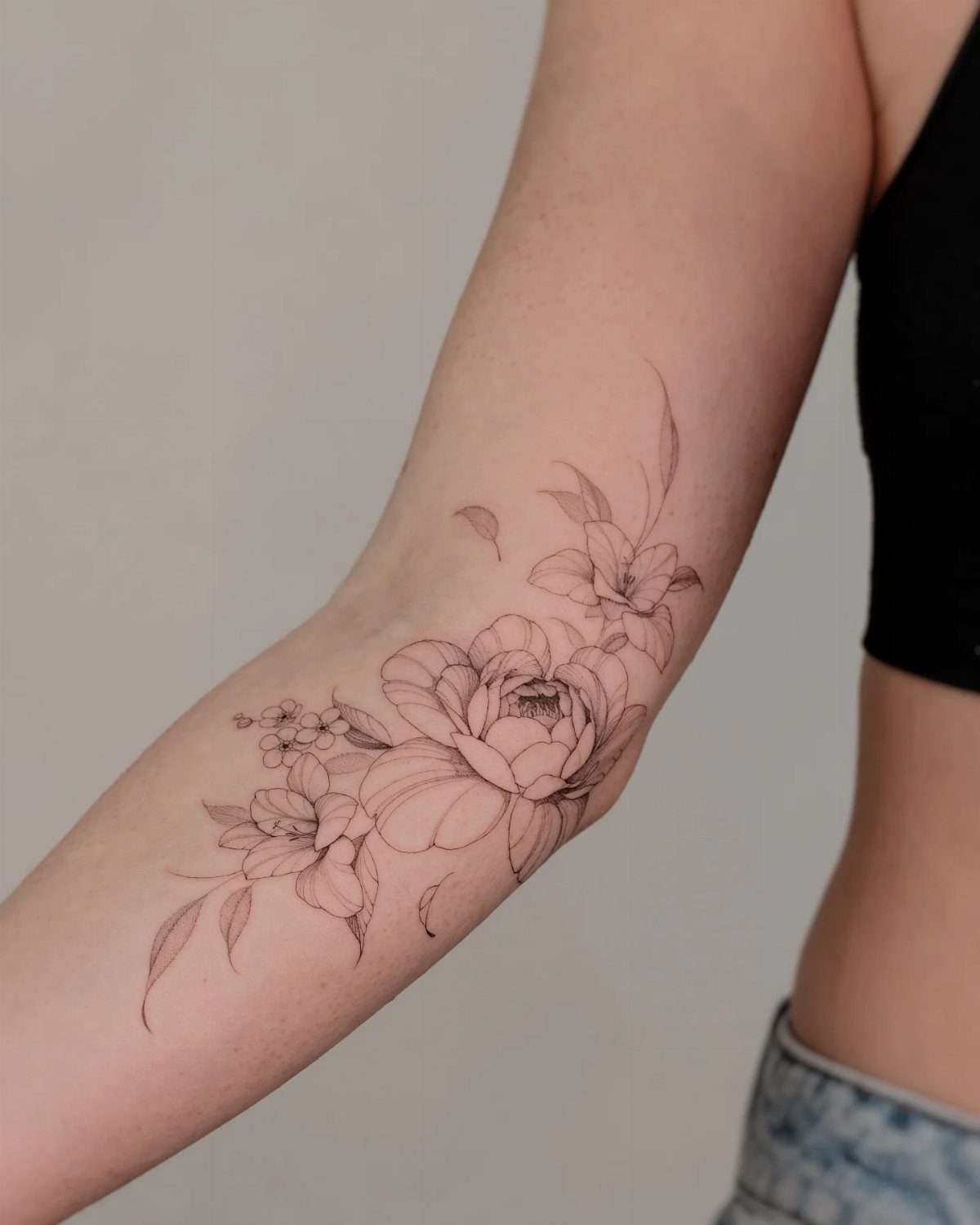 A black ink fine line peony floral arrangement tattoo on a person's forearm.