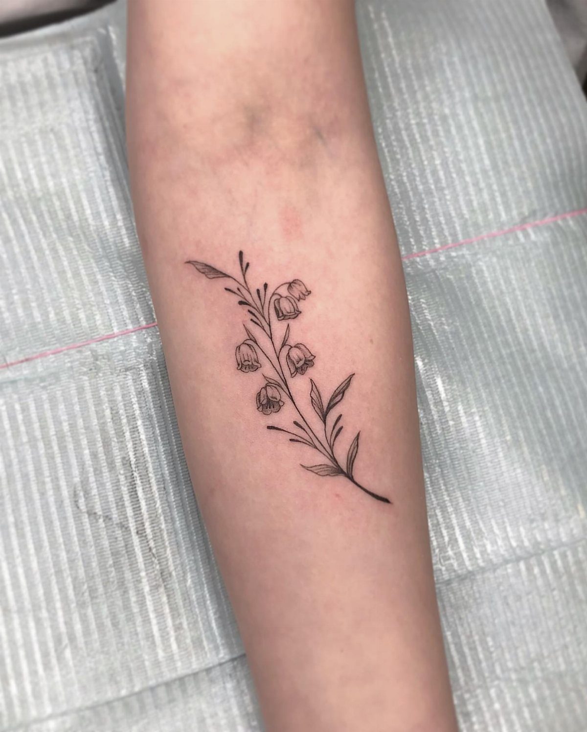 A delicate black ink Lily of the Valley floral tattoo on a person's forearm.