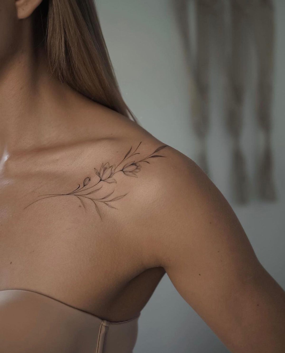 A delicate fine line floral tattoo on a person's shoulder and collarbone.