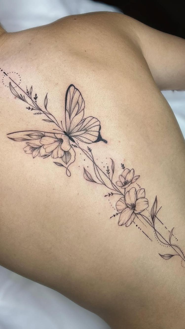 A black ink butterfly and floral vine tattoo running down a person's spine.