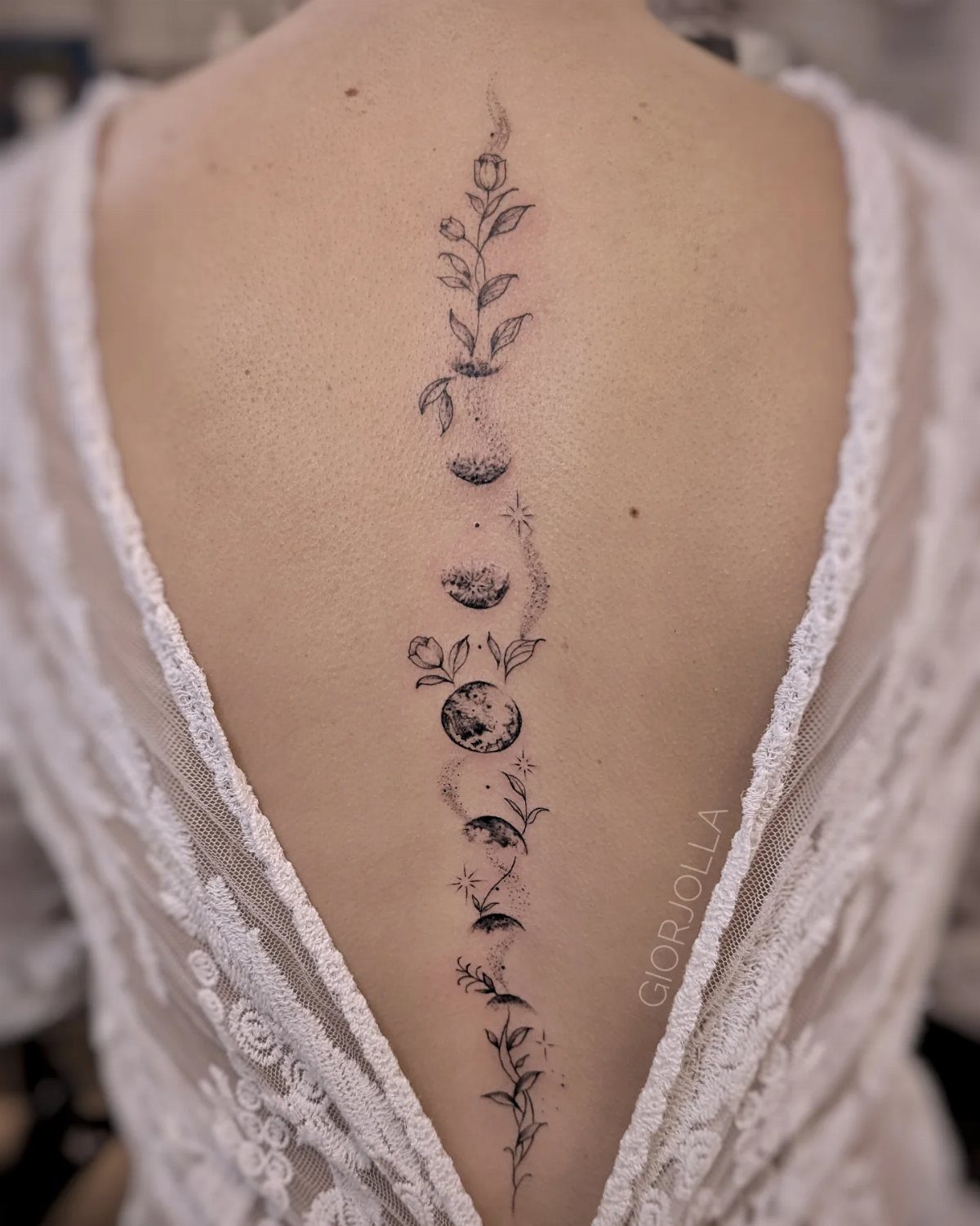 A vertical spine tattoo depicting moon phases intertwined with delicate leaves and floral line art.