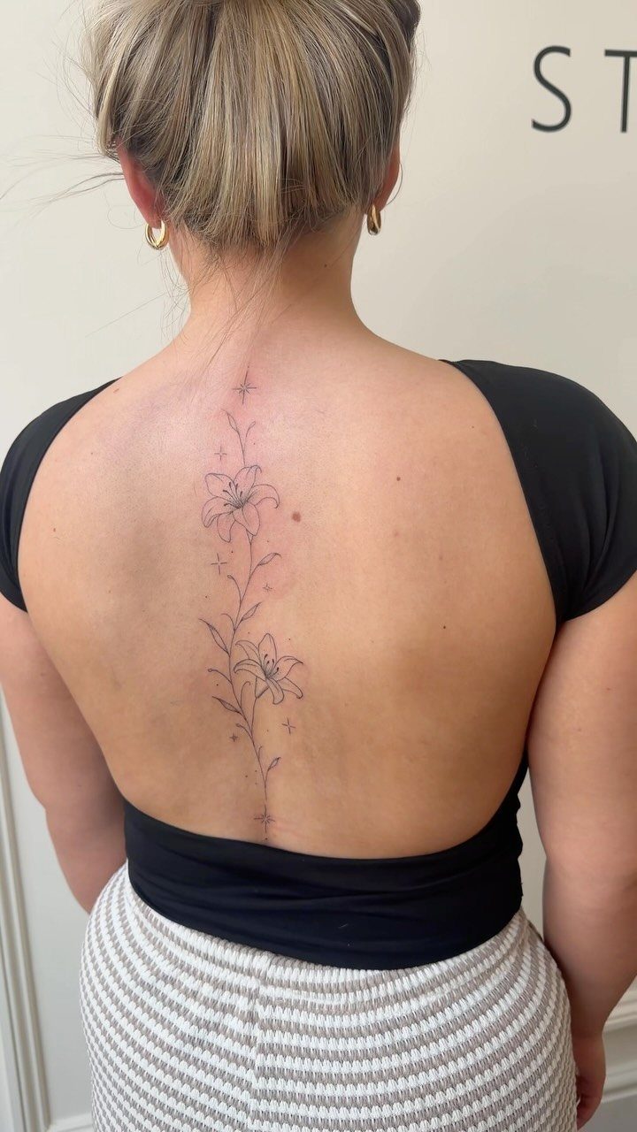 A fine line floral tattoo running vertically down a person's spine.