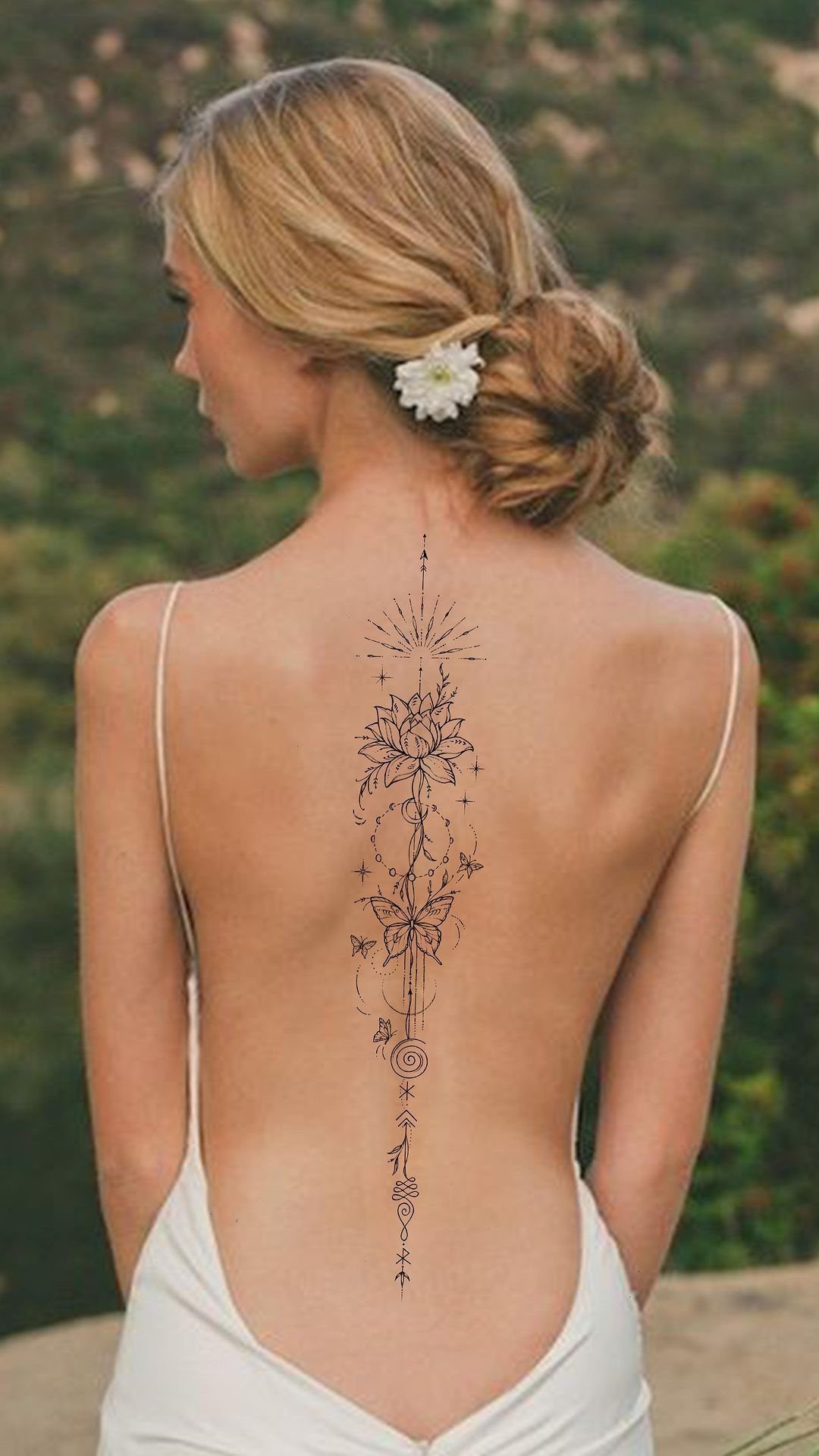 A woman's back featuring a long, vertical floral and geometric tattoo running down her spine.